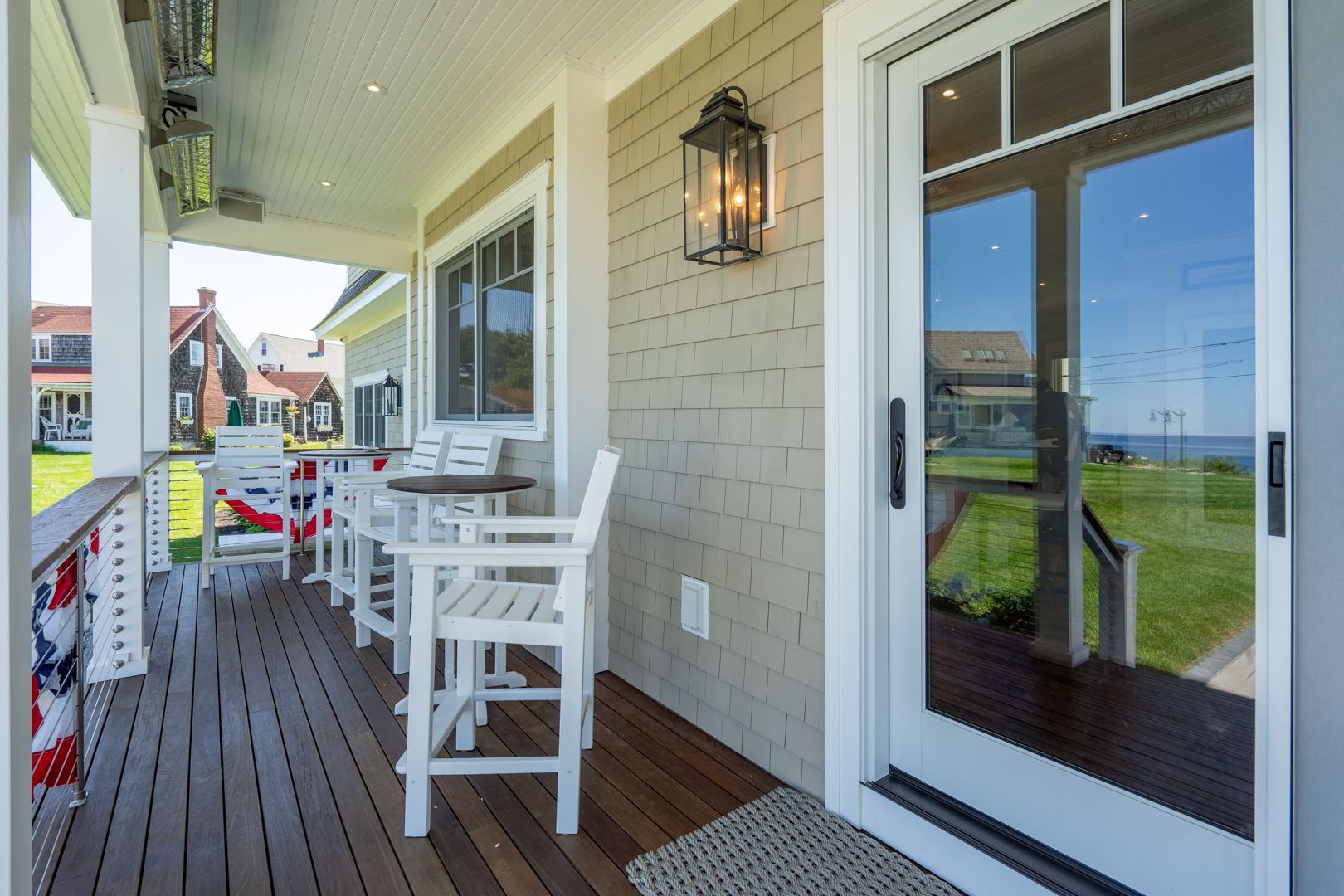 Porch with white chairs, wooden floor, and glass doors overlooking a grassy waterfront.