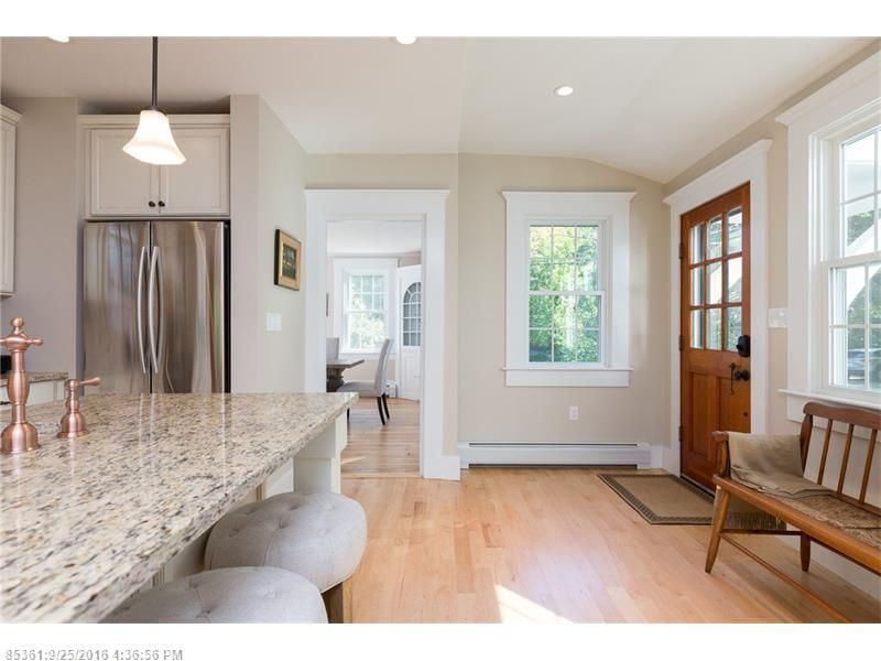 Bright kitchen with granite island, stainless fridge, hardwood floors, and wood front door.