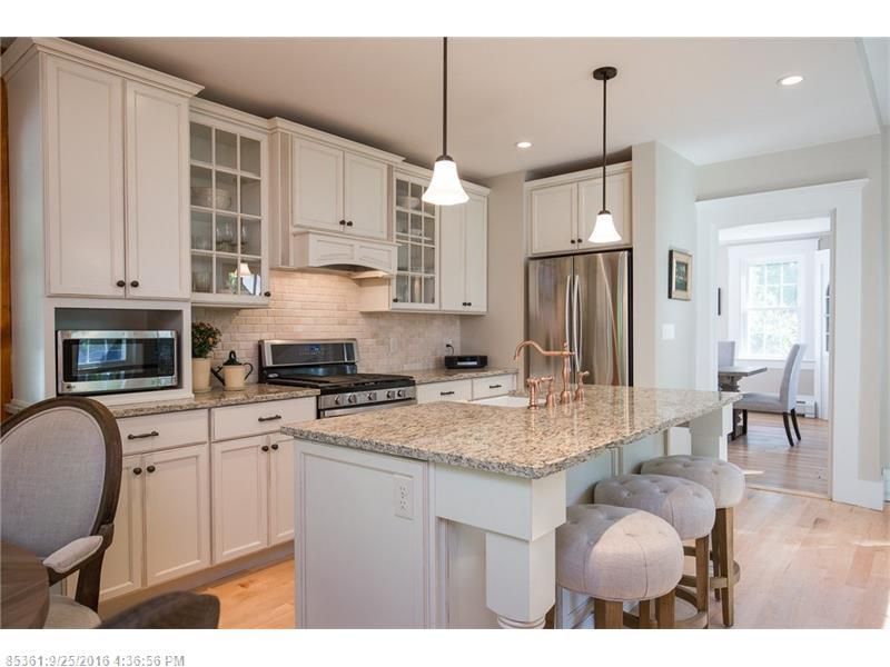 Bright modern kitchen with white cabinets, granite island, pendant lights, and stainless steel appliances