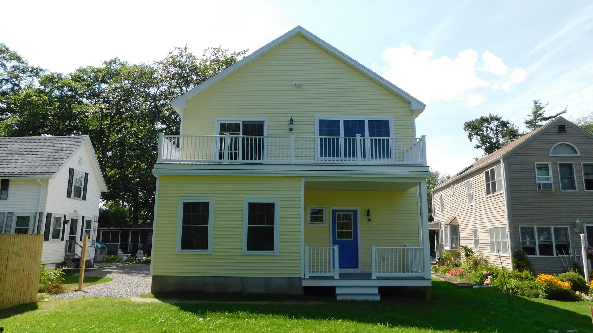 Yellow two-story house with blue trim and porch, centered on a grassy lawn, with neighboring homes nearby
