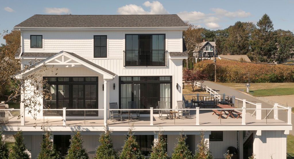 Modern two-story white house with black-framed windows, a large patio, and a waterfront view