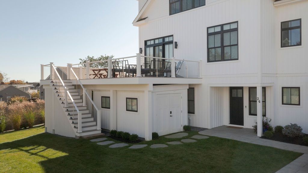 White house exterior with upper deck, outdoor staircase, patio doors, and green lawn