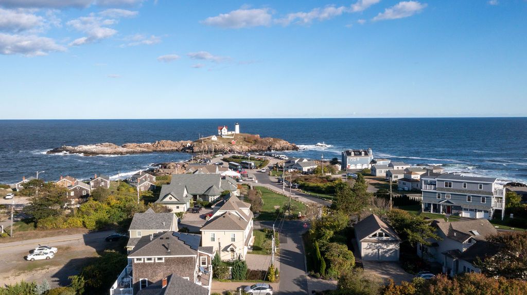 Coastal town view with houses in the foreground, a harbor, and the ocean under a bright blue sky
