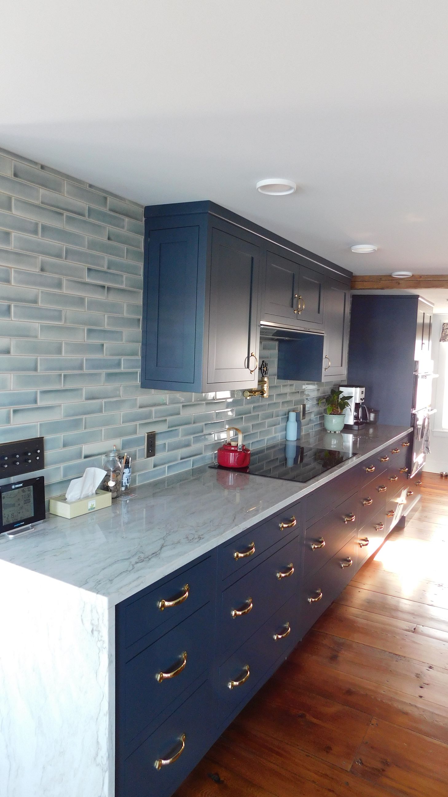 Modern kitchen with dark blue cabinets, light countertop, gray brick backsplash, and wooden floor.