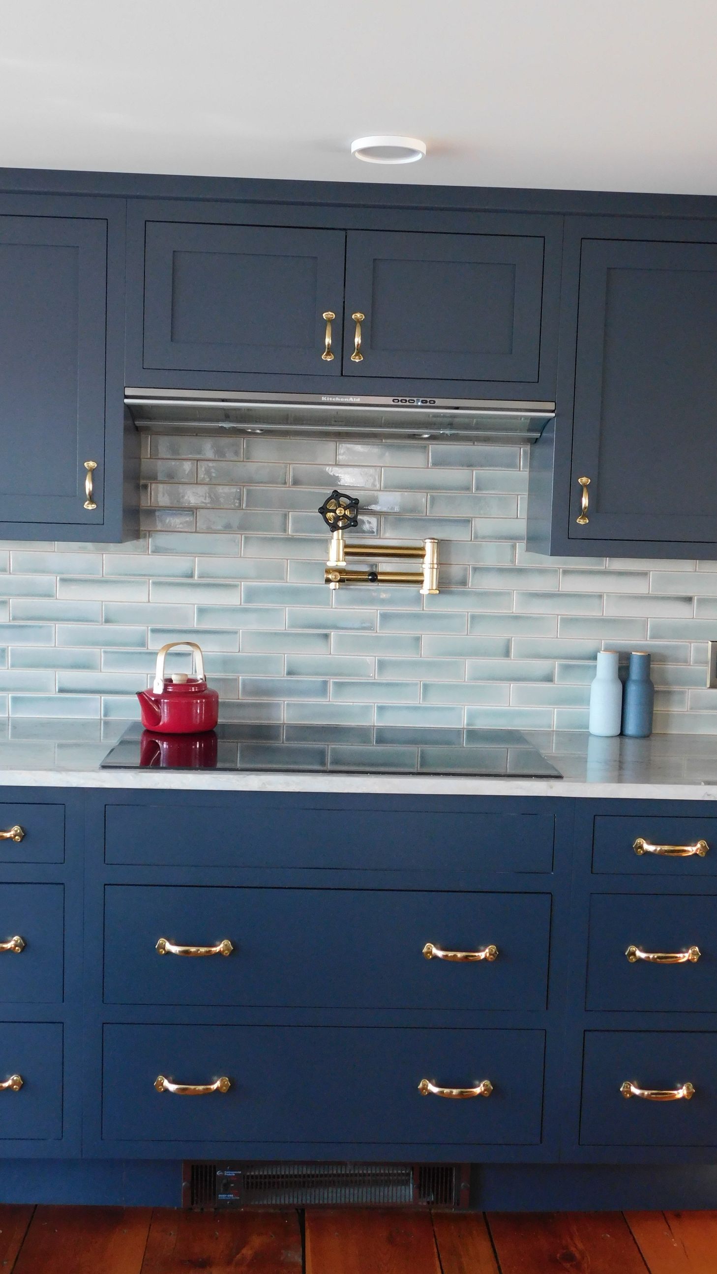 Blue kitchen cabinets with brass handles and a light blue tile backsplash above a sink counter.