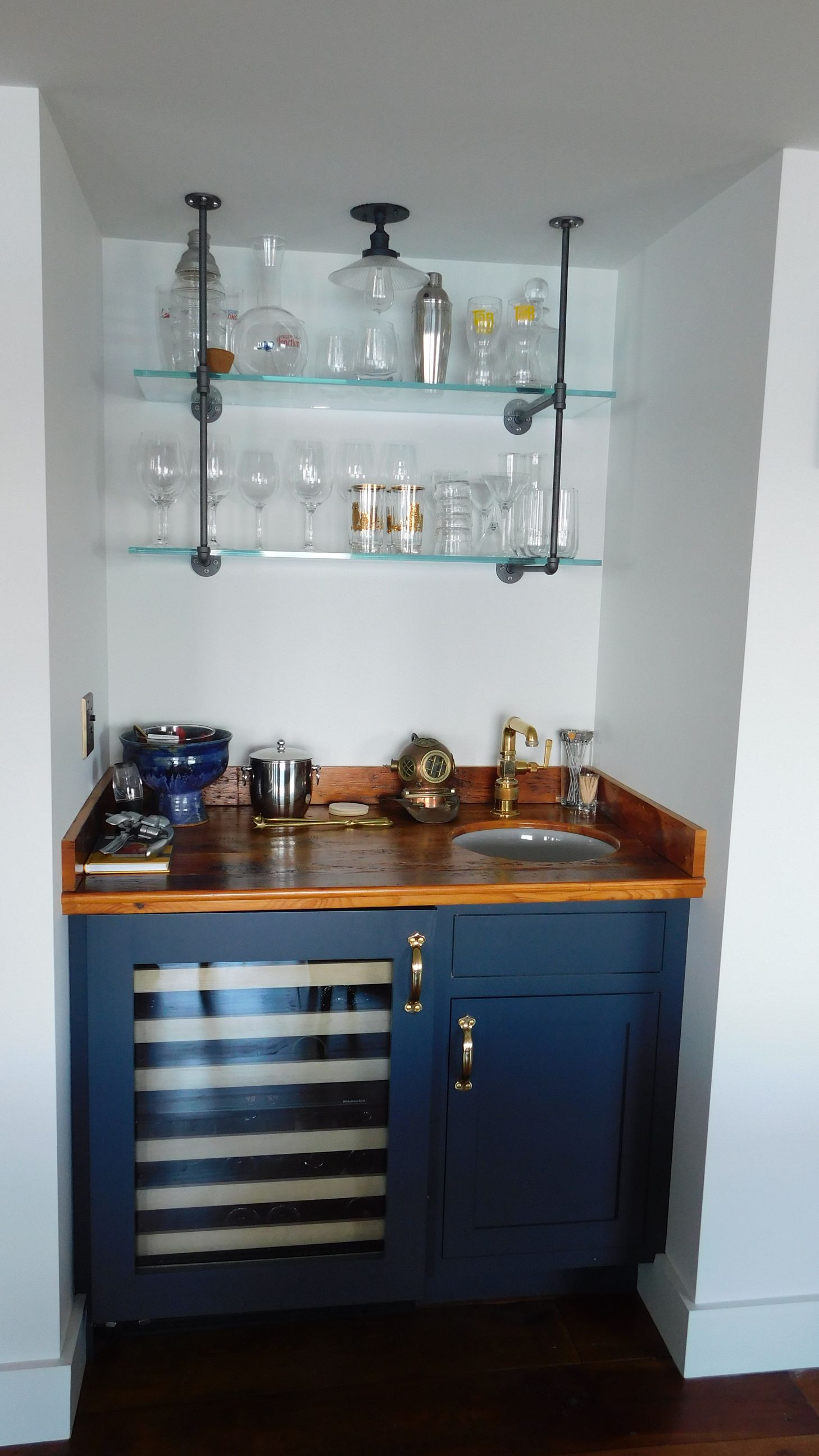 Compact bar nook with blue cabinets, wooden countertop, shelves, and glassware in a small alcove