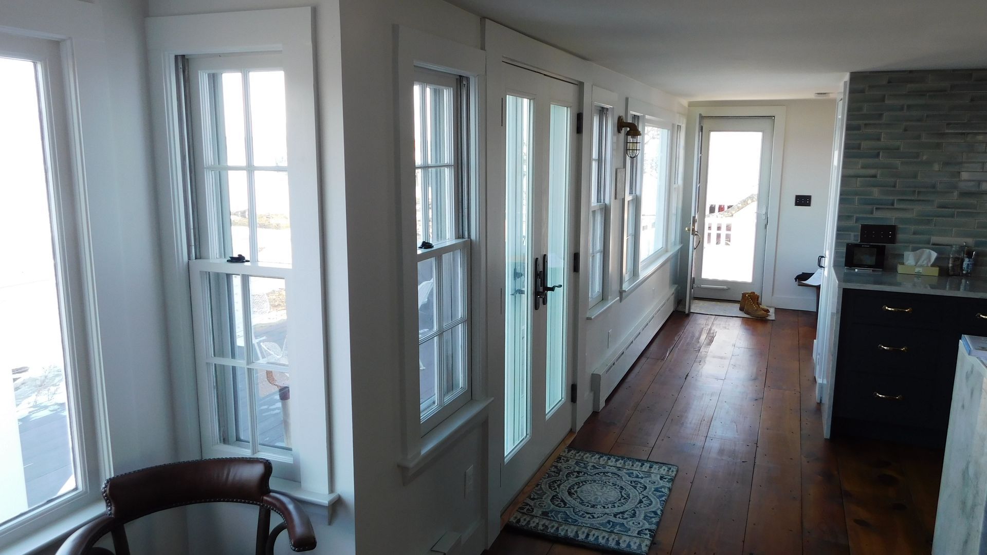 Bright hallway with white doors and windows, hardwood floor, rug, and a dark kitchen counter on the right.