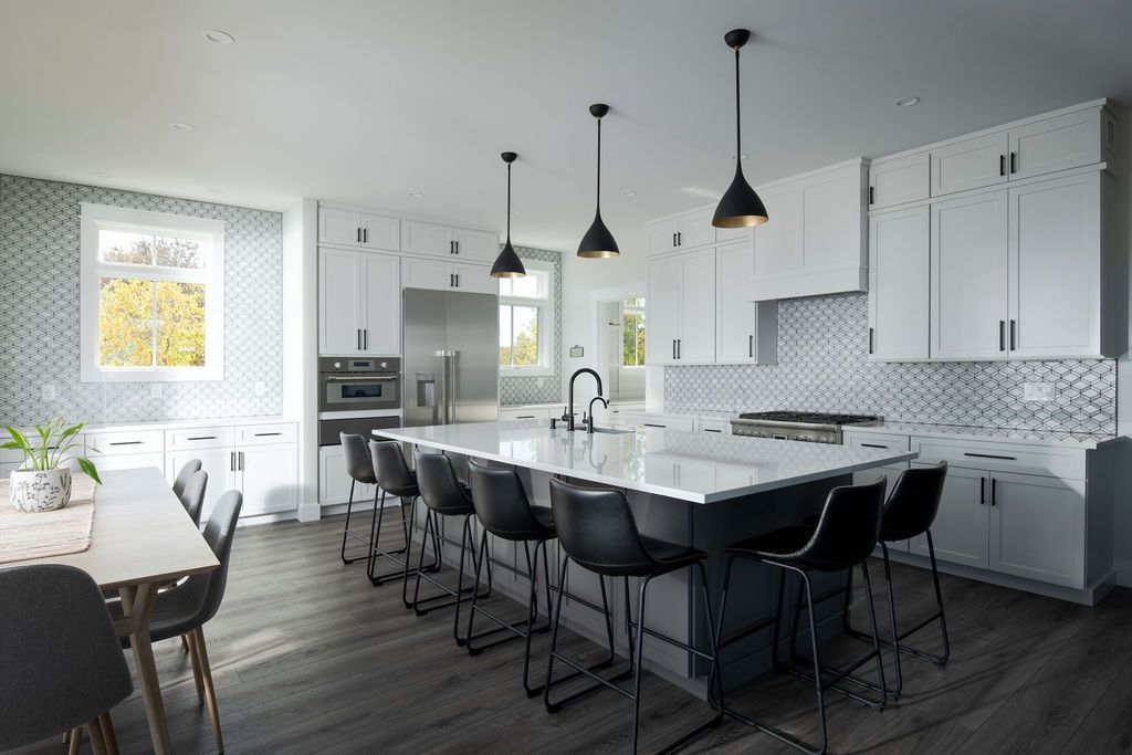 Modern white kitchen with large island, black barstools, pendant lights, and mosaic backsplash