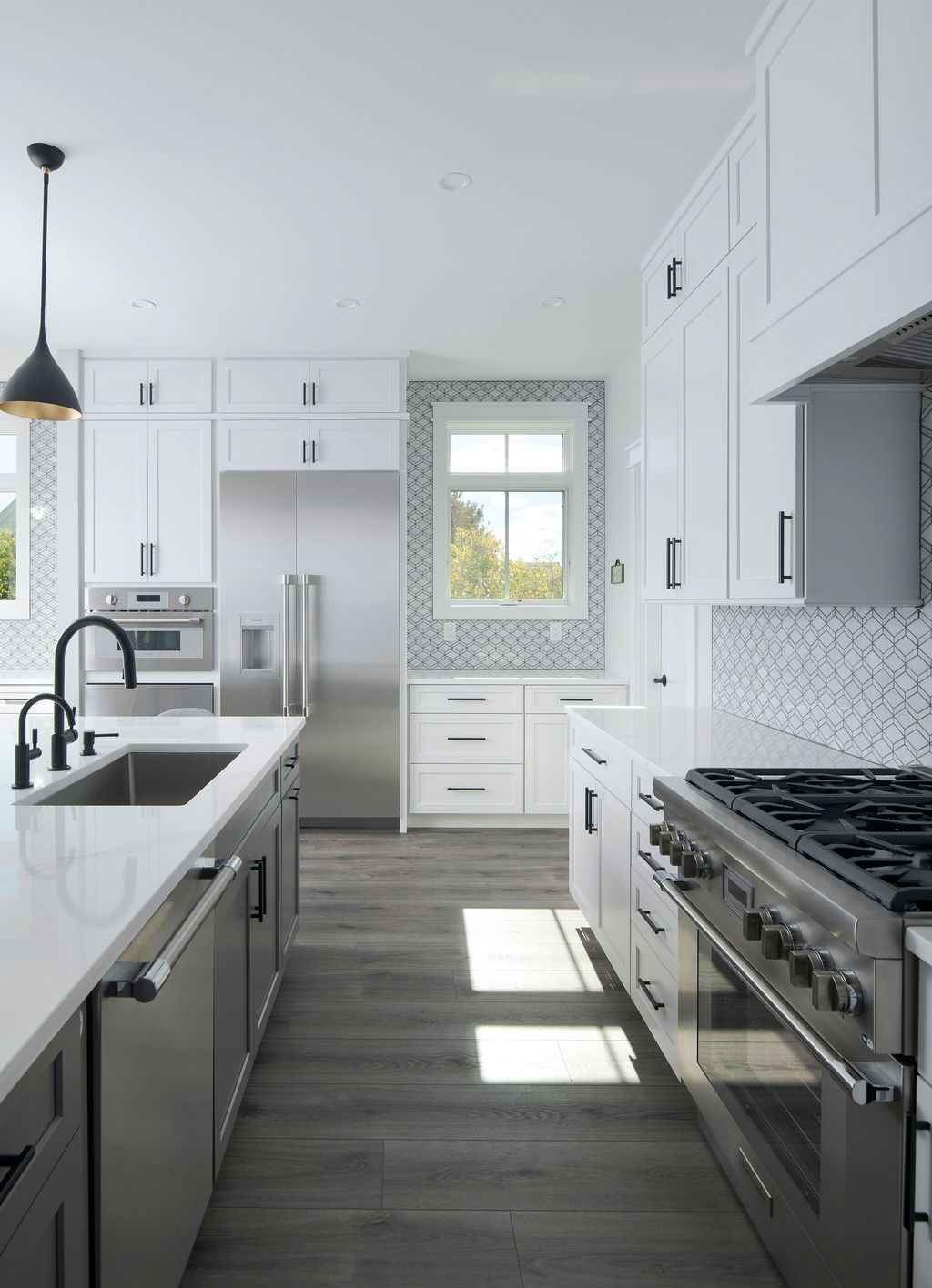 Modern white kitchen with gray island, stainless appliances, and sunlight on wood floors