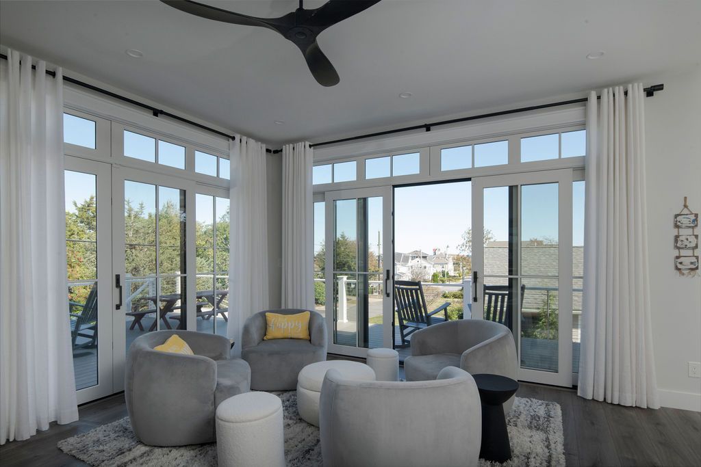 Bright living room with gray chairs, white curtains, and large windows overlooking a balcony and ocean view
