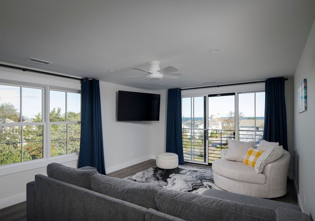 Modern living room with large windows, dark blue curtains, gray sofa, white chair, and wall-mounted TV