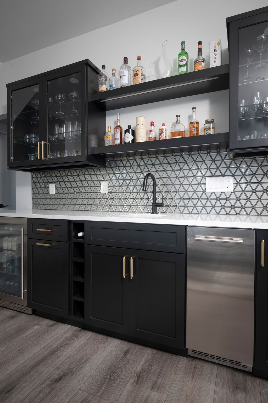 Modern black home bar with glass-front cabinets, open shelves, and stainless-steel mini fridge under patterned backsplash