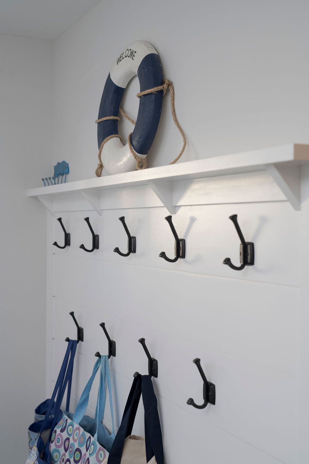 White wall shelf with hanging hooks holding bags, blue flip-flops, and a life preserver.