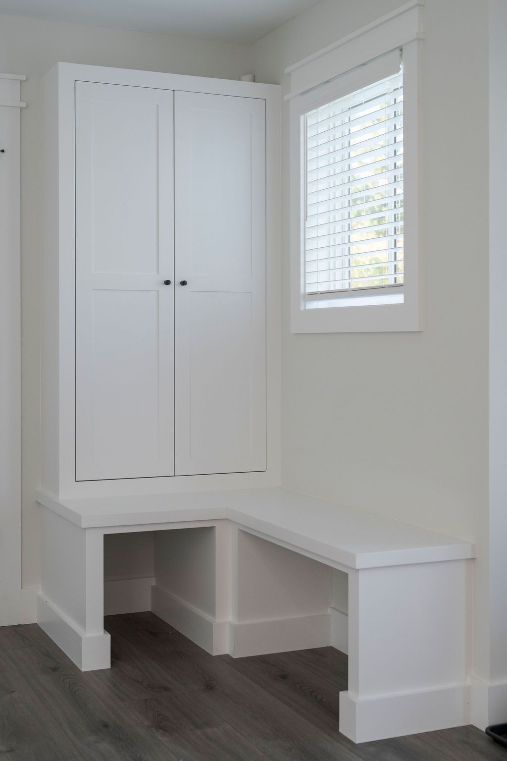 White built-in corner desk with cabinets beside a window in a bright room