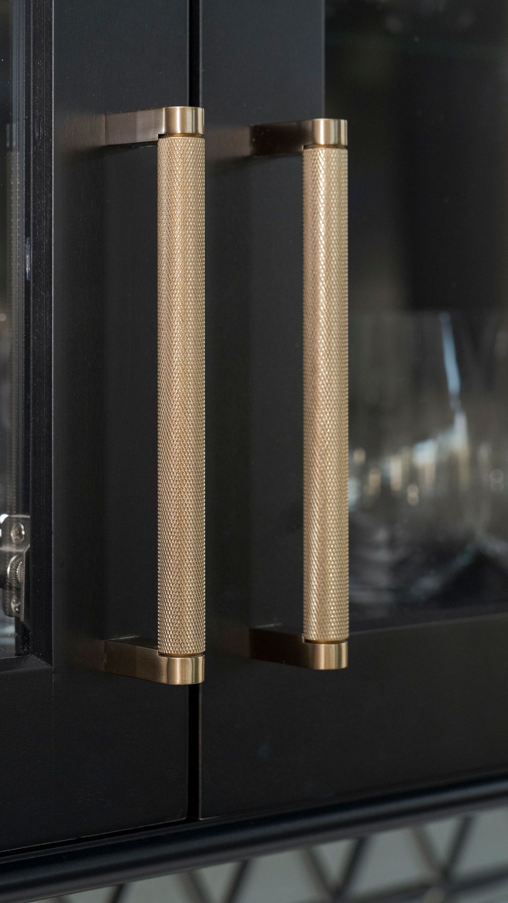 Close-up of gold textured handles on a black glass cabinet door