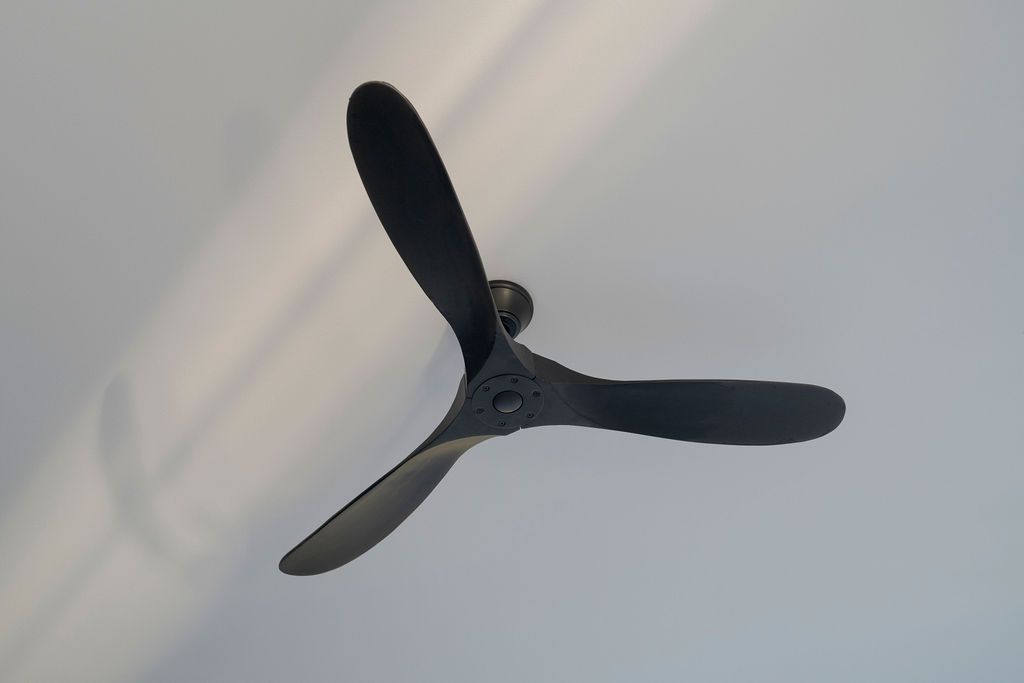 Dark ceiling fan with three blades against a light ceiling
