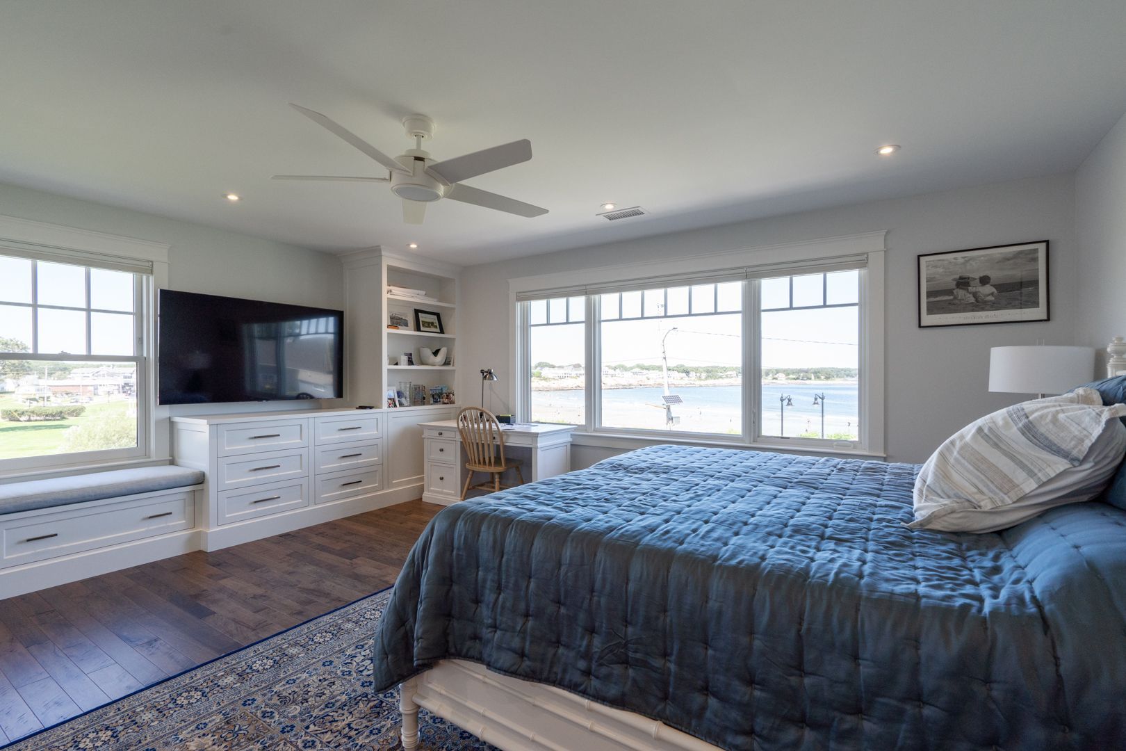 Bright bedroom with a large bed, TV, white dresser, and windows overlooking water.