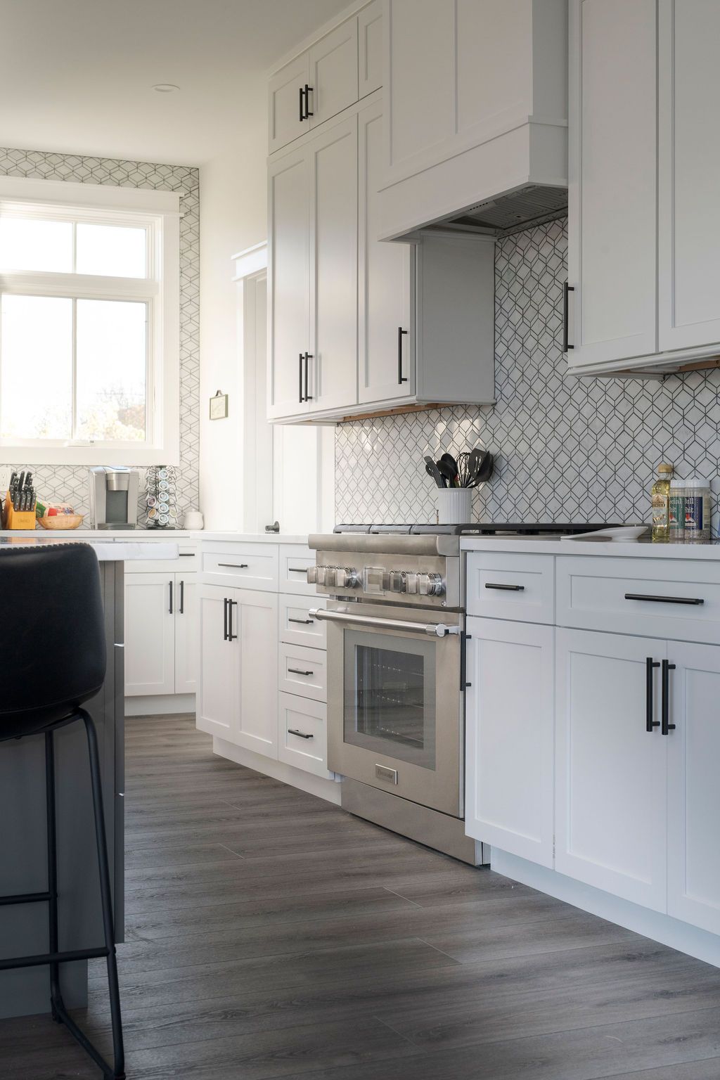 Modern white kitchen with stainless steel stove, patterned backsplash, and gray wood flooring