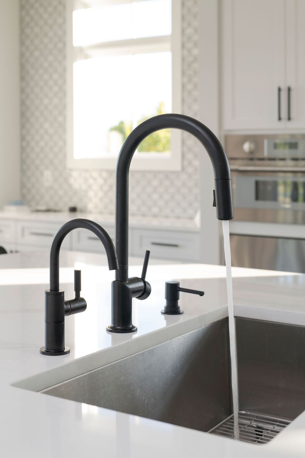 Modern kitchen sink with black faucet and white countertops by a bright window