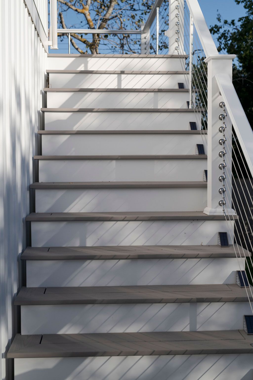 White outdoor staircase with black railings leading up toward a deck under a blue sky