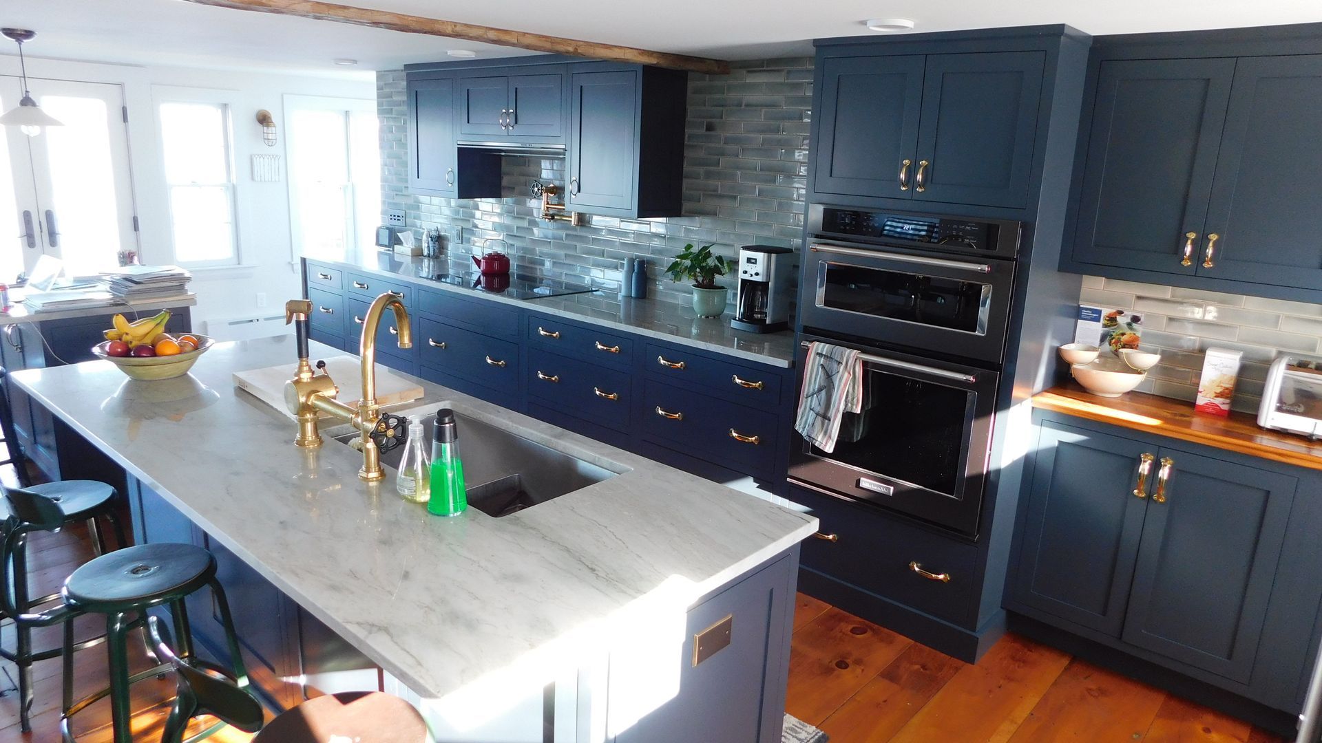 Bright modern kitchen with blue cabinets, white island, stainless appliances, and wooden floors.