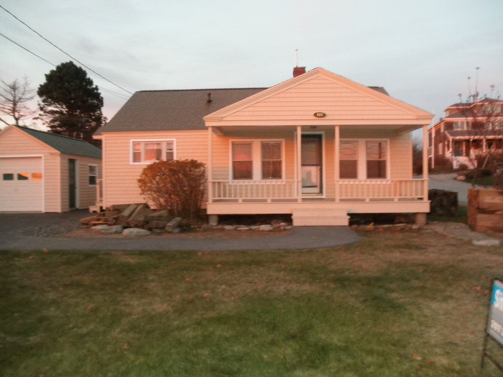 Single-story beige house with a front porch, small lawn, and garage at dusk