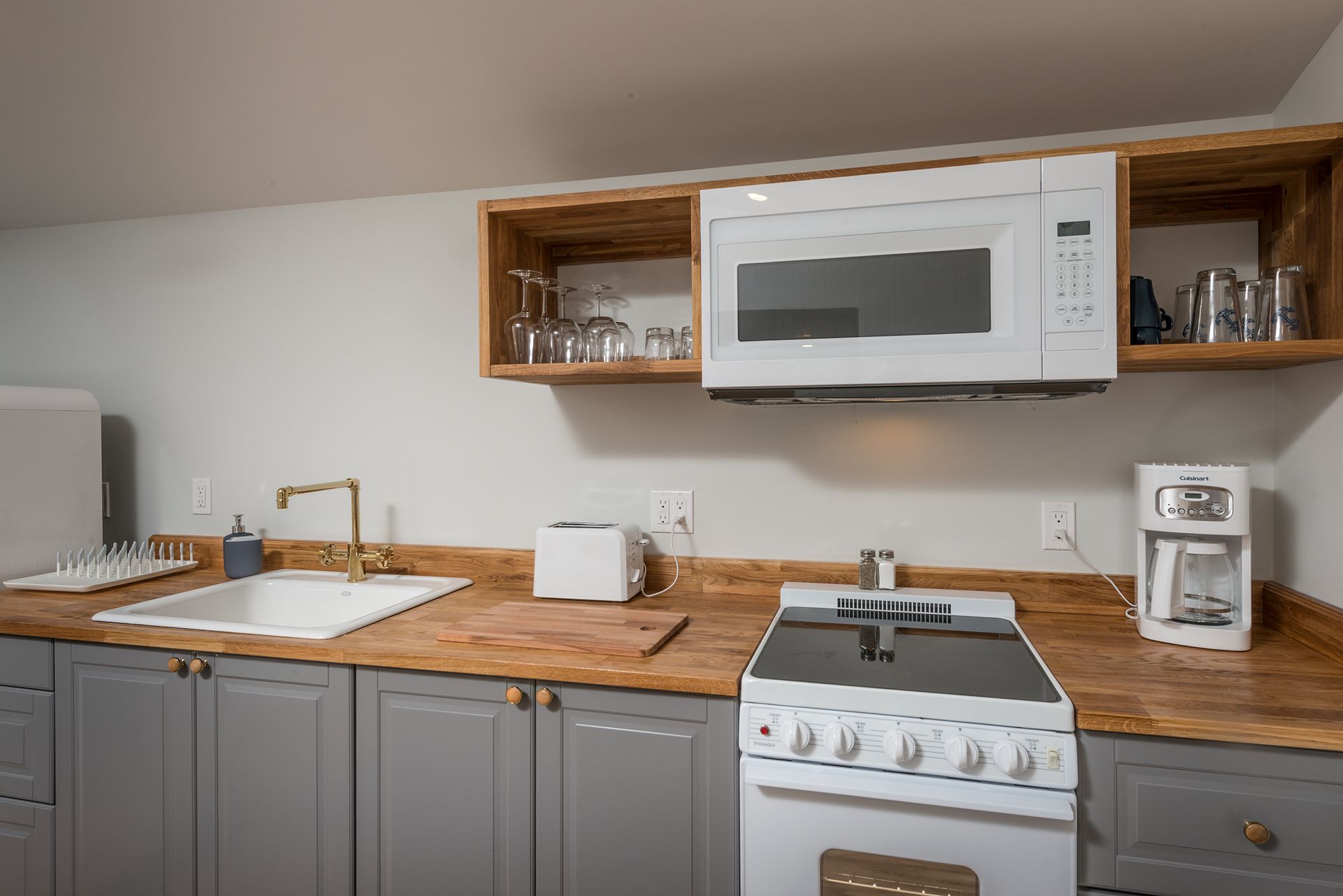 Modern kitchen with gray cabinets, wood countertops, white stove, microwave, sink, and coffee maker
