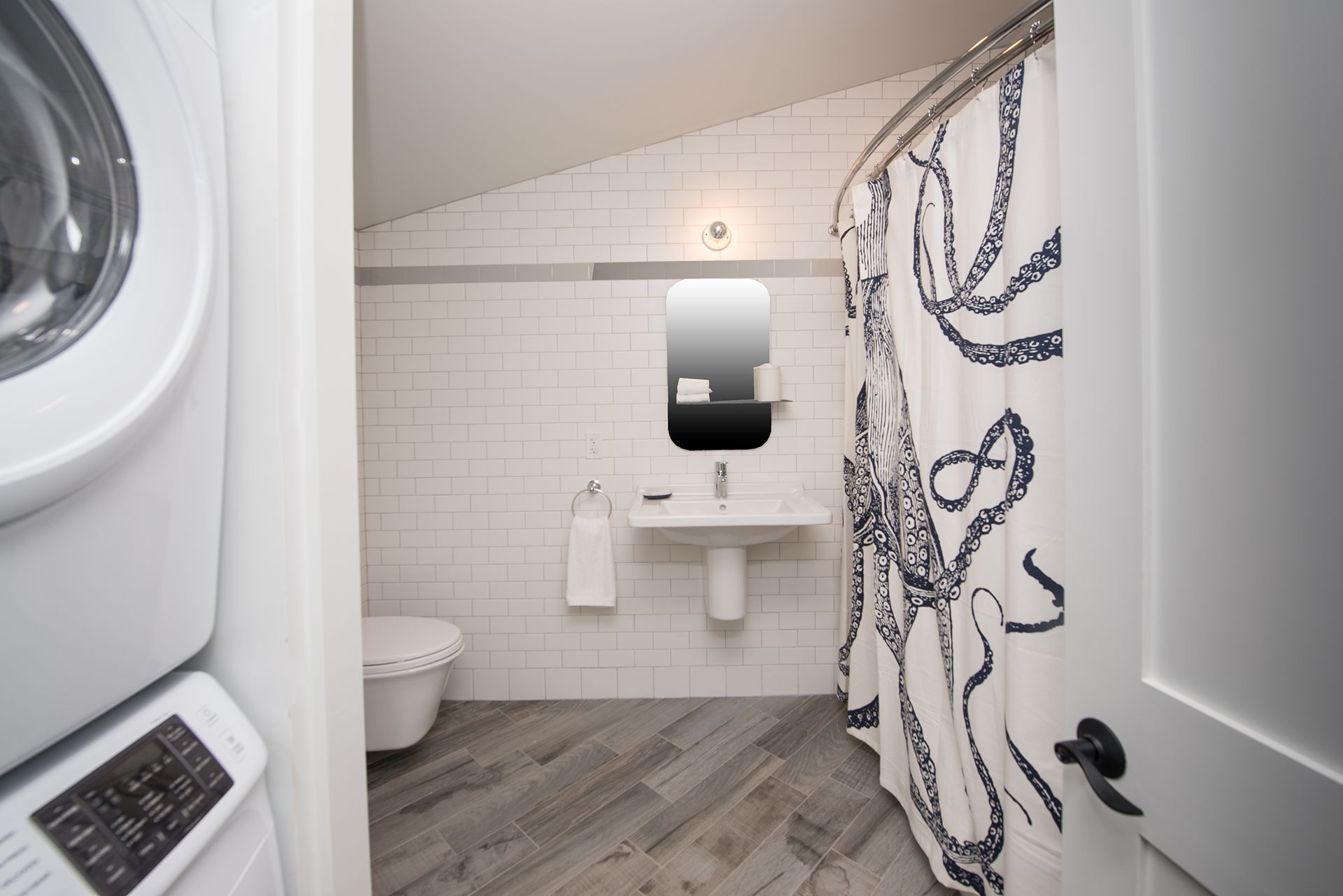 Small bathroom with a toilet, sink, mirror, washer, and octopus shower curtain.