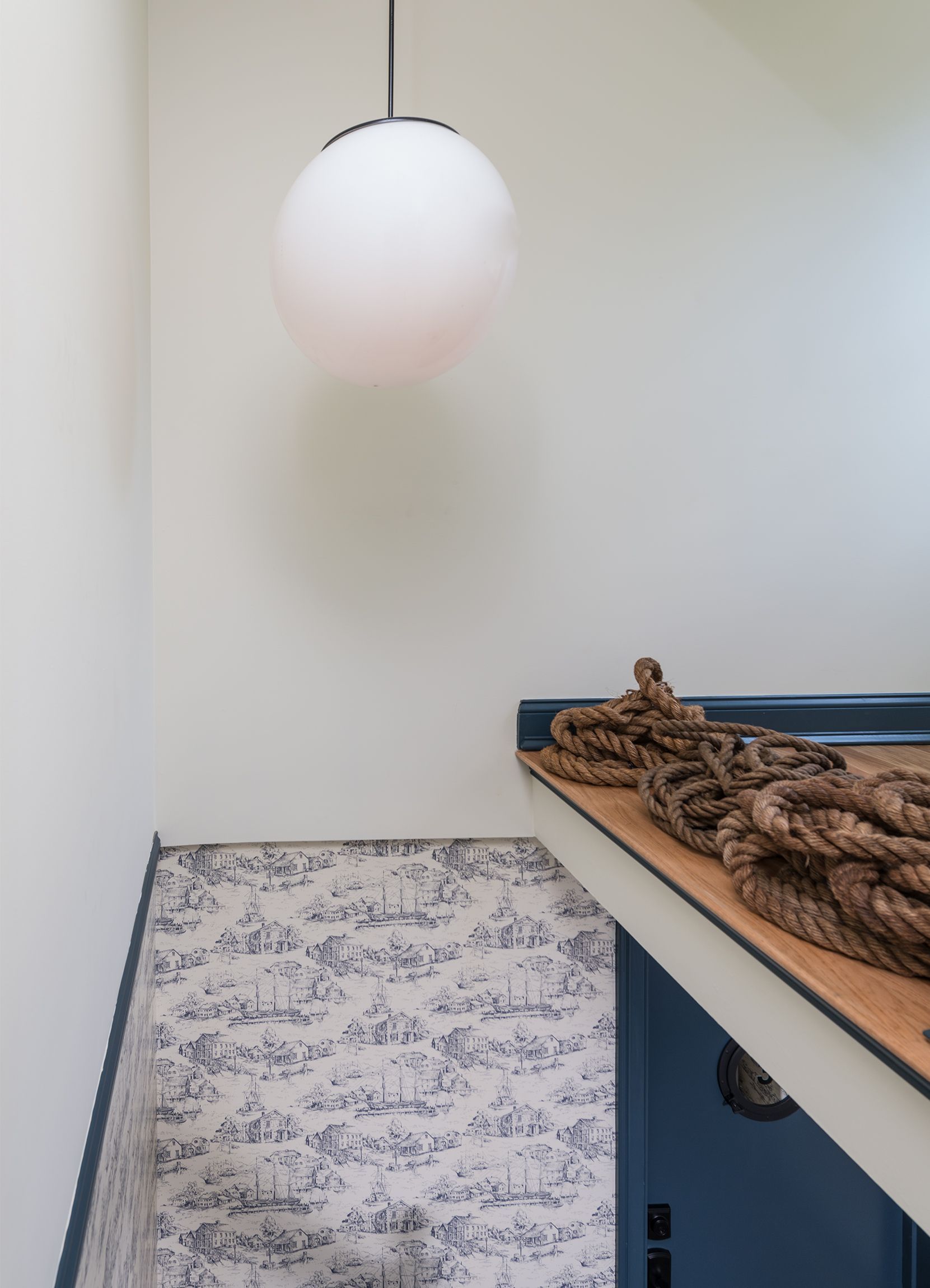 White pendant lamp above a patterned rug and a wooden shelf with rope in a minimalist corner