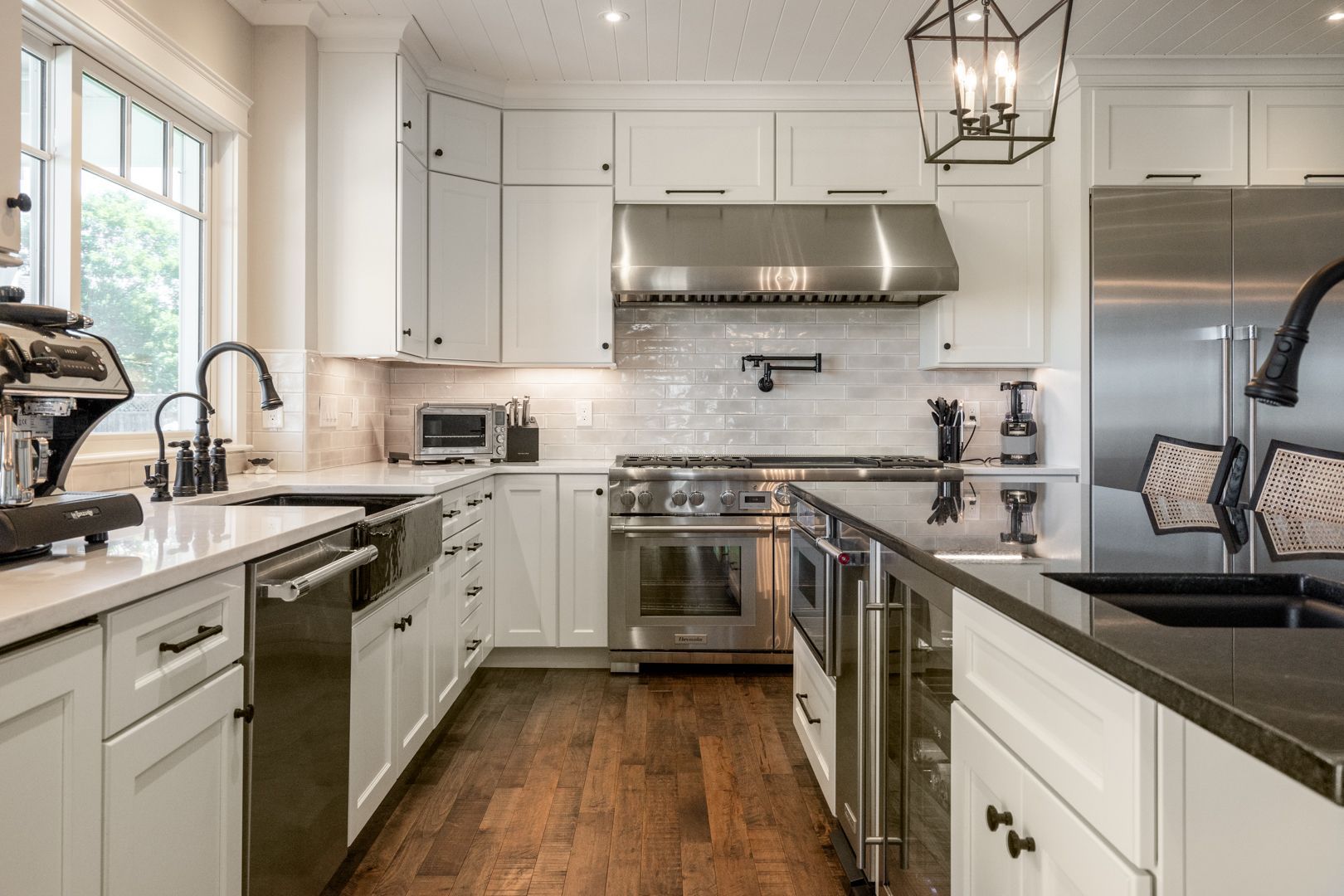 Bright white kitchen with stainless steel appliances, wood floor, and black countertops