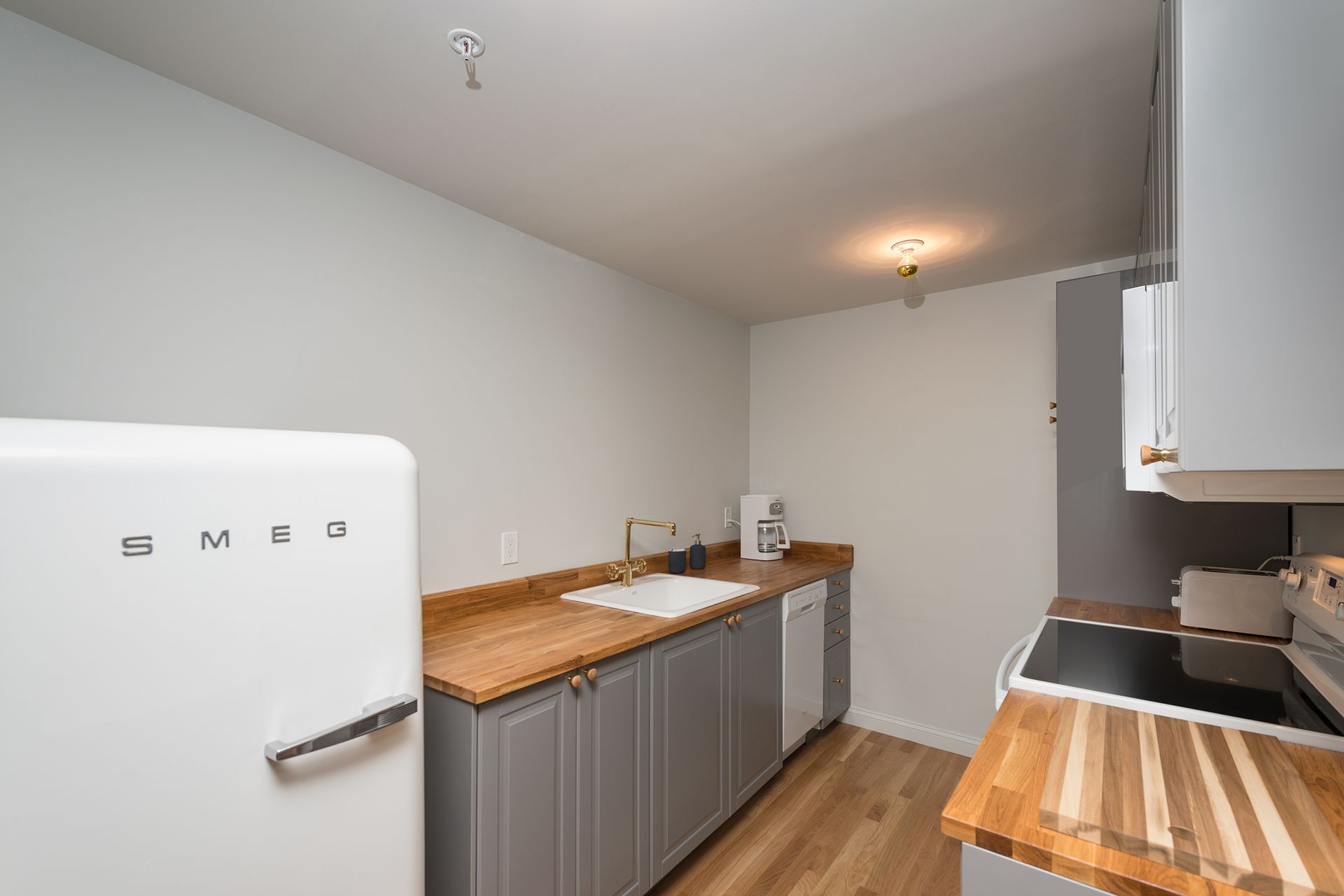 Small kitchen with white fridge, gray cabinets, wood countertops, and hardwood floor under soft lighting