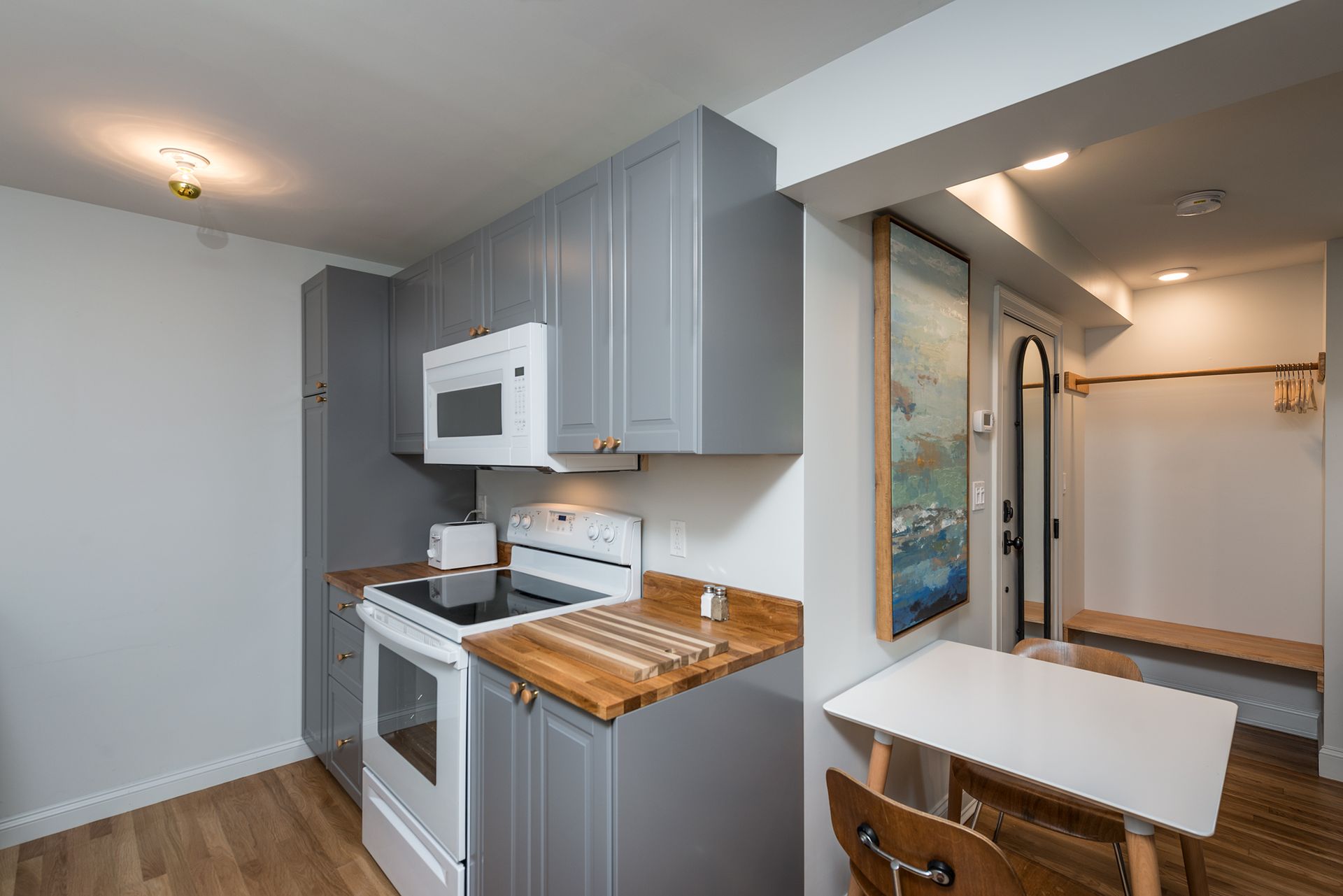 Small gray kitchen with white appliances, wood countertops, and a narrow dining area by the hallway.