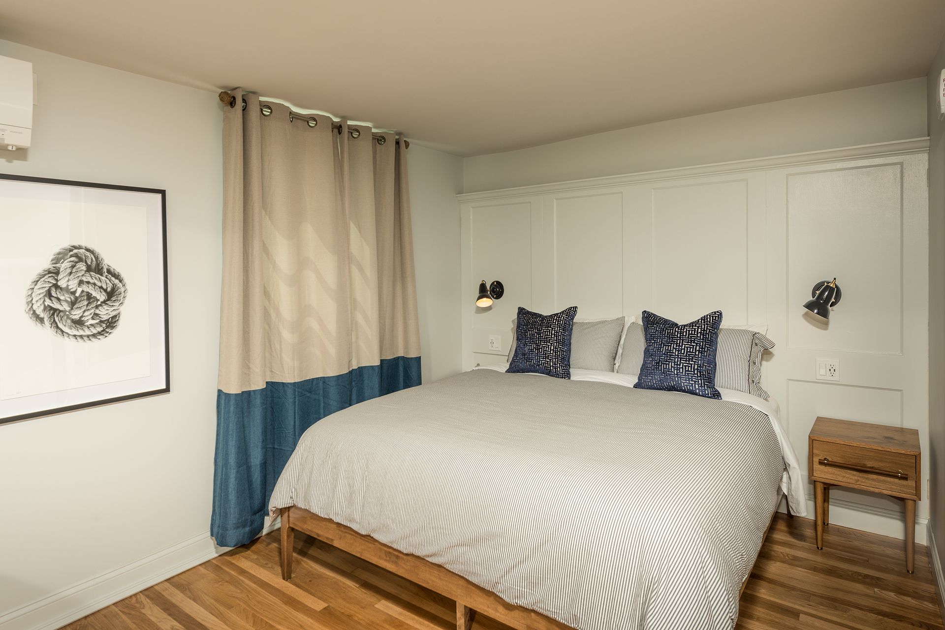 Neat bedroom with a bed, patterned bedding, bedside table, curtains, and wall art