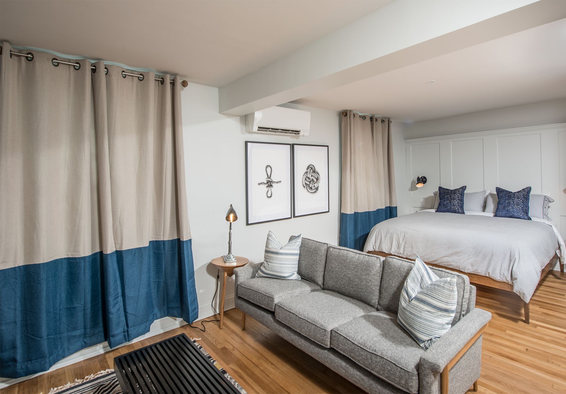 Modern bedroom with gray sofa, blue-and-beige curtains, and a bed against the wall