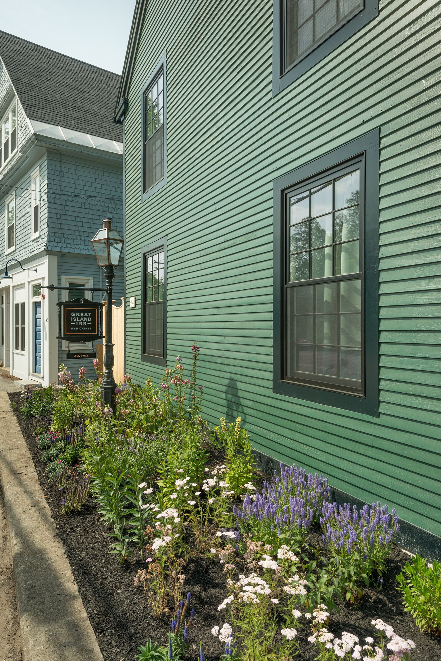 Green clapboard house with black-trimmed windows and a flower bed along a narrow walkway