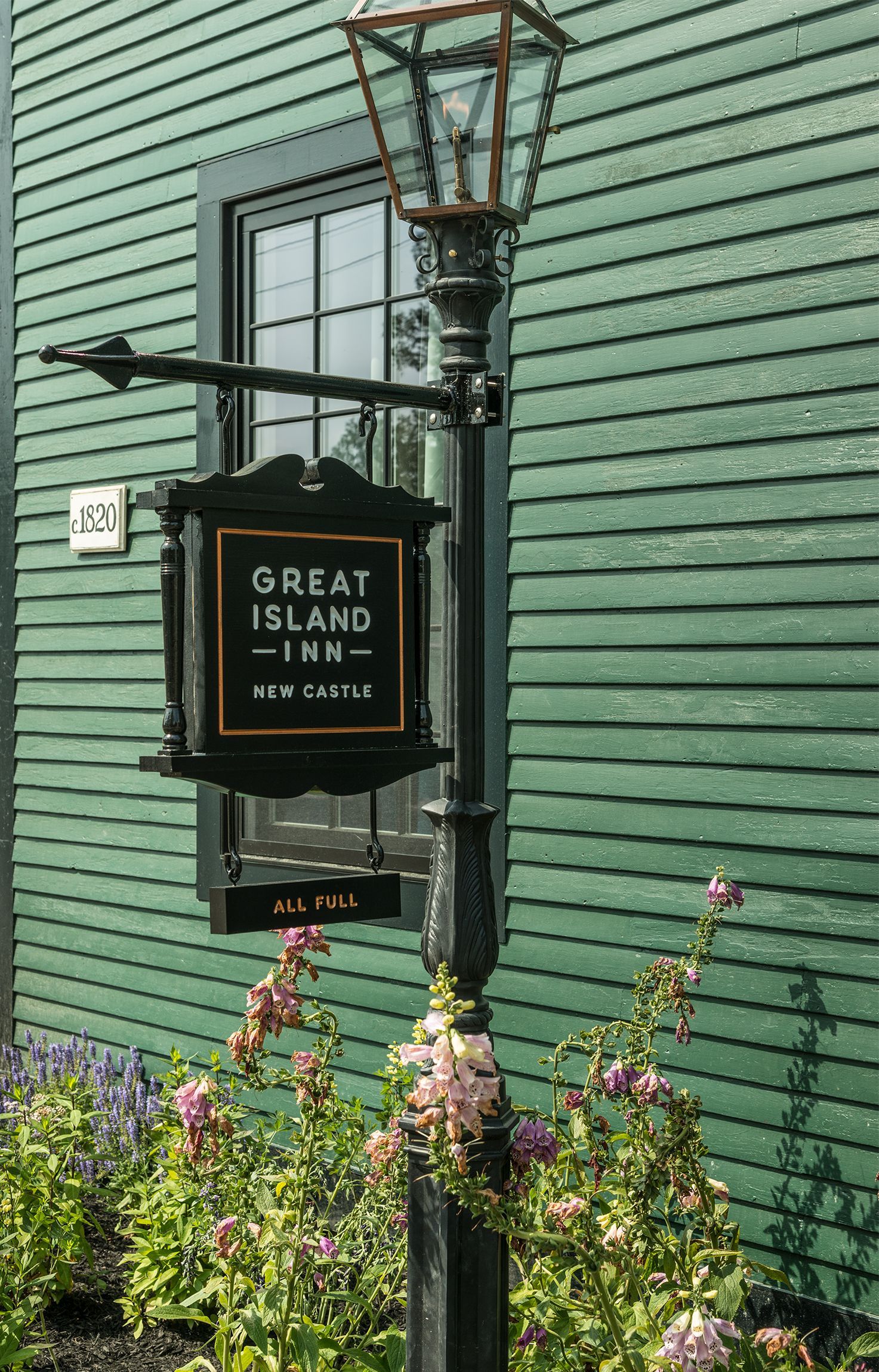 Great Island Inn sign on a green clapboard building, with a lamp post and flowers in front