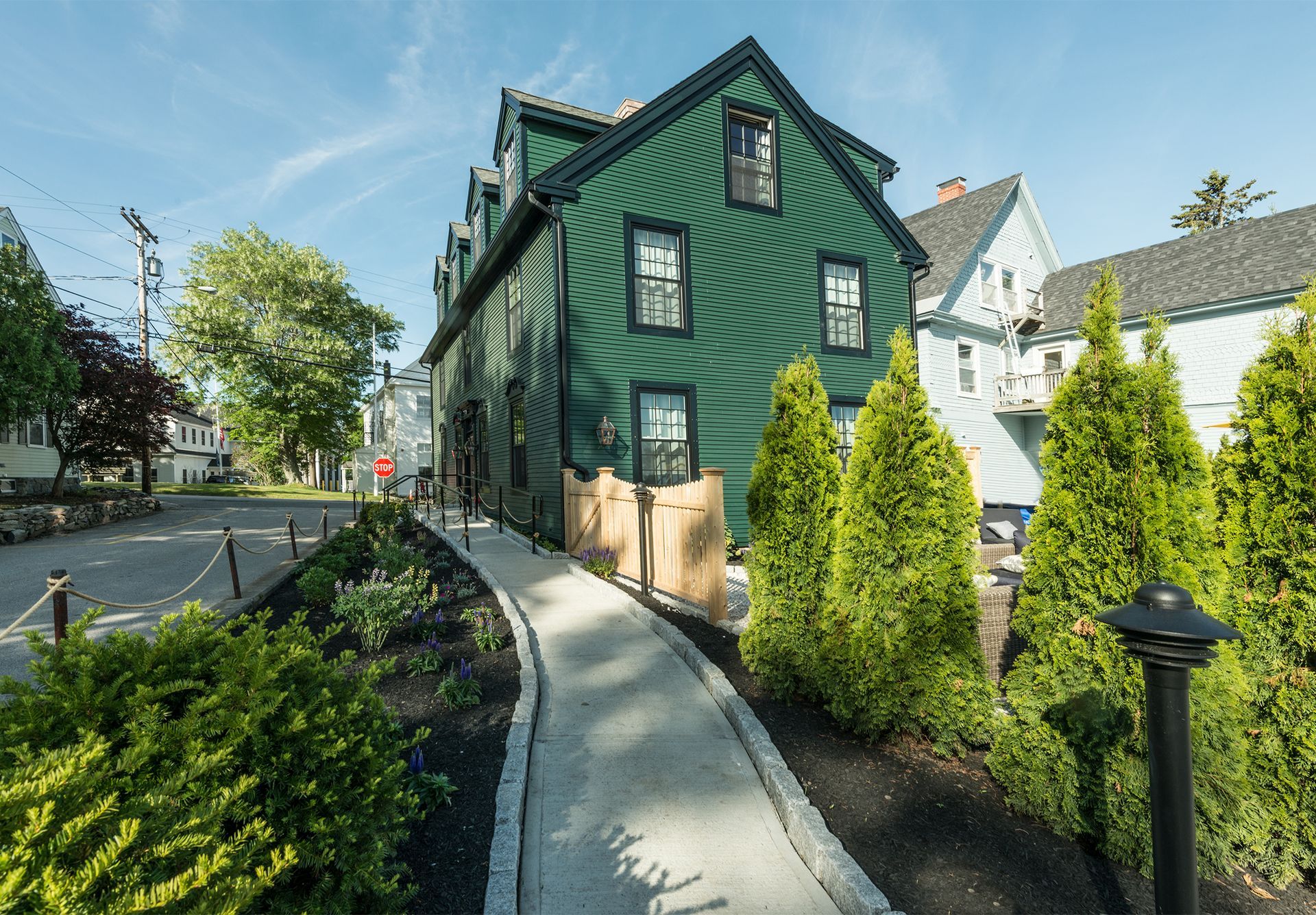 Green house with a curved sidewalk, shrubs, and a quiet residential street on a sunny day