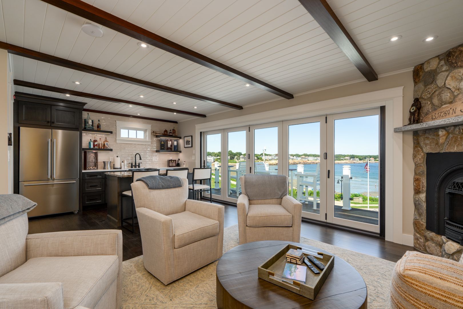 Bright living room with large windows, beige chairs, a stone fireplace, and an ocean view