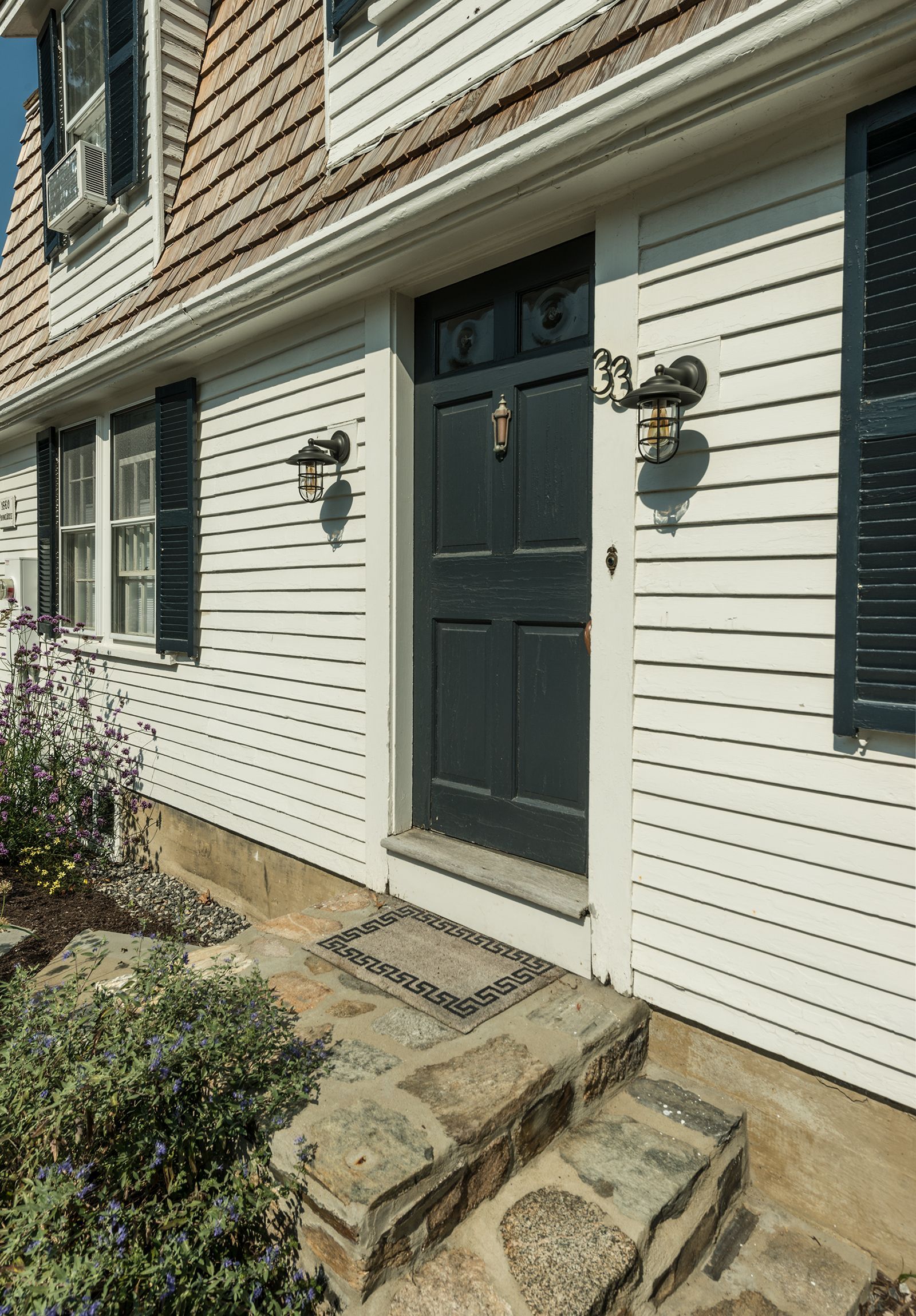 Front entrance of a house with white siding, a dark door, stone steps, and black shutters.