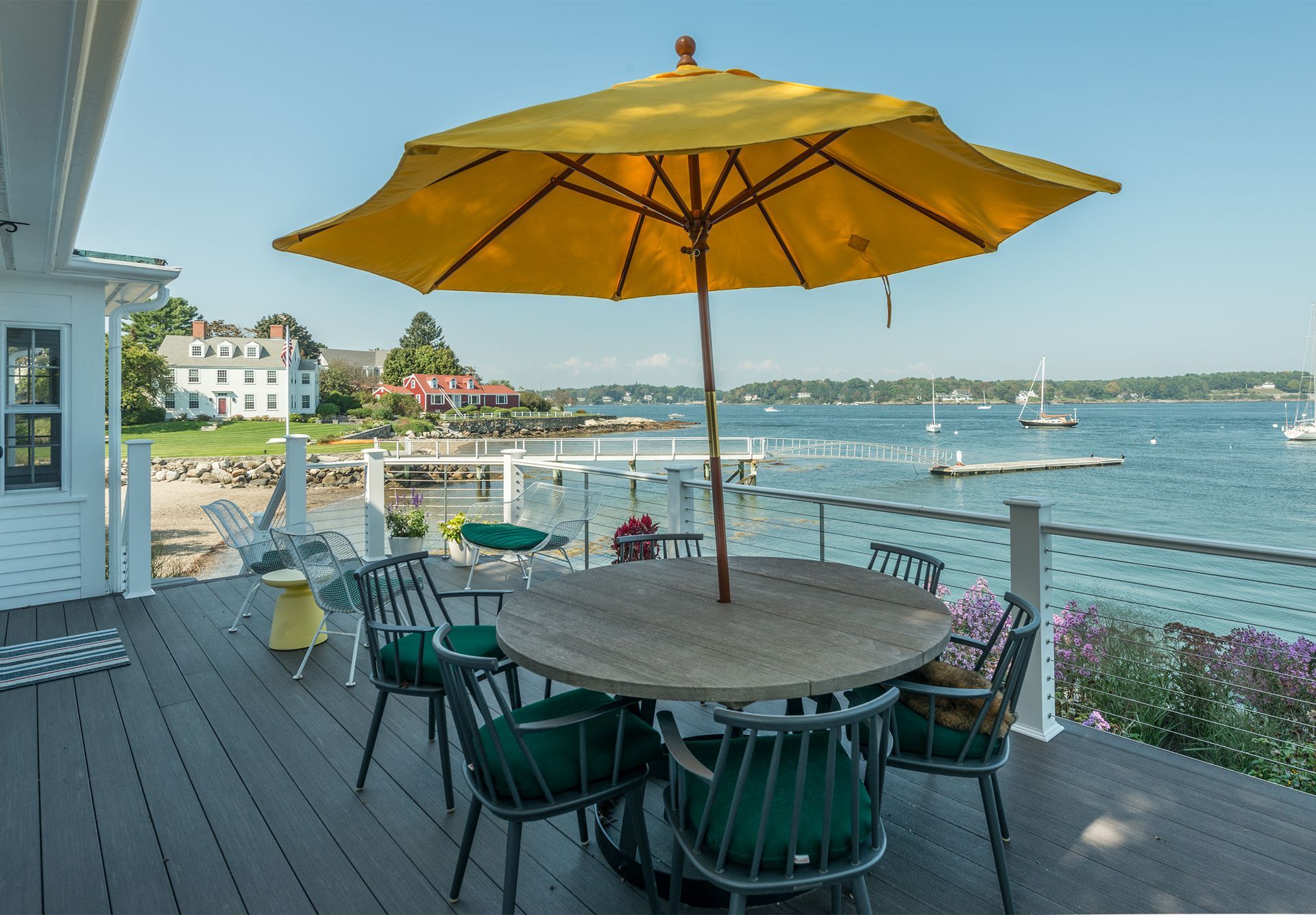 Waterfront patio with yellow umbrella, round table, and chairs overlooking a calm harbor.