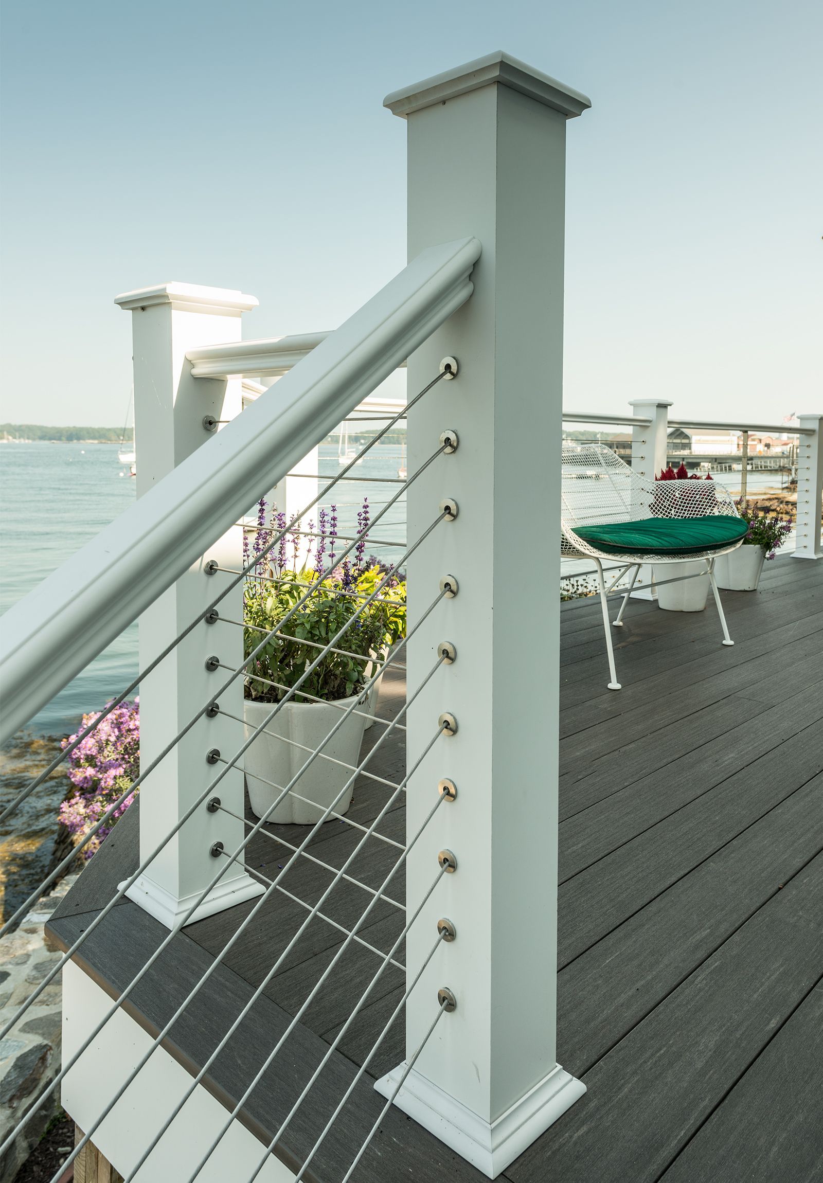 White cable railing on a waterfront deck with planters and chairs overlooking the water