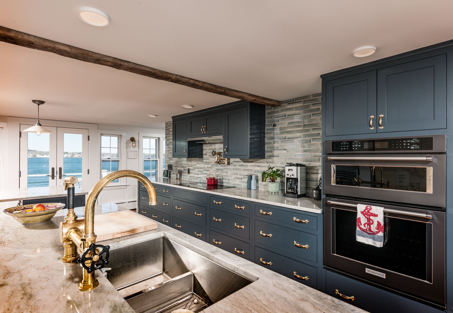 Modern kitchen with navy cabinets, stone backsplash, gold faucet, and double ovens