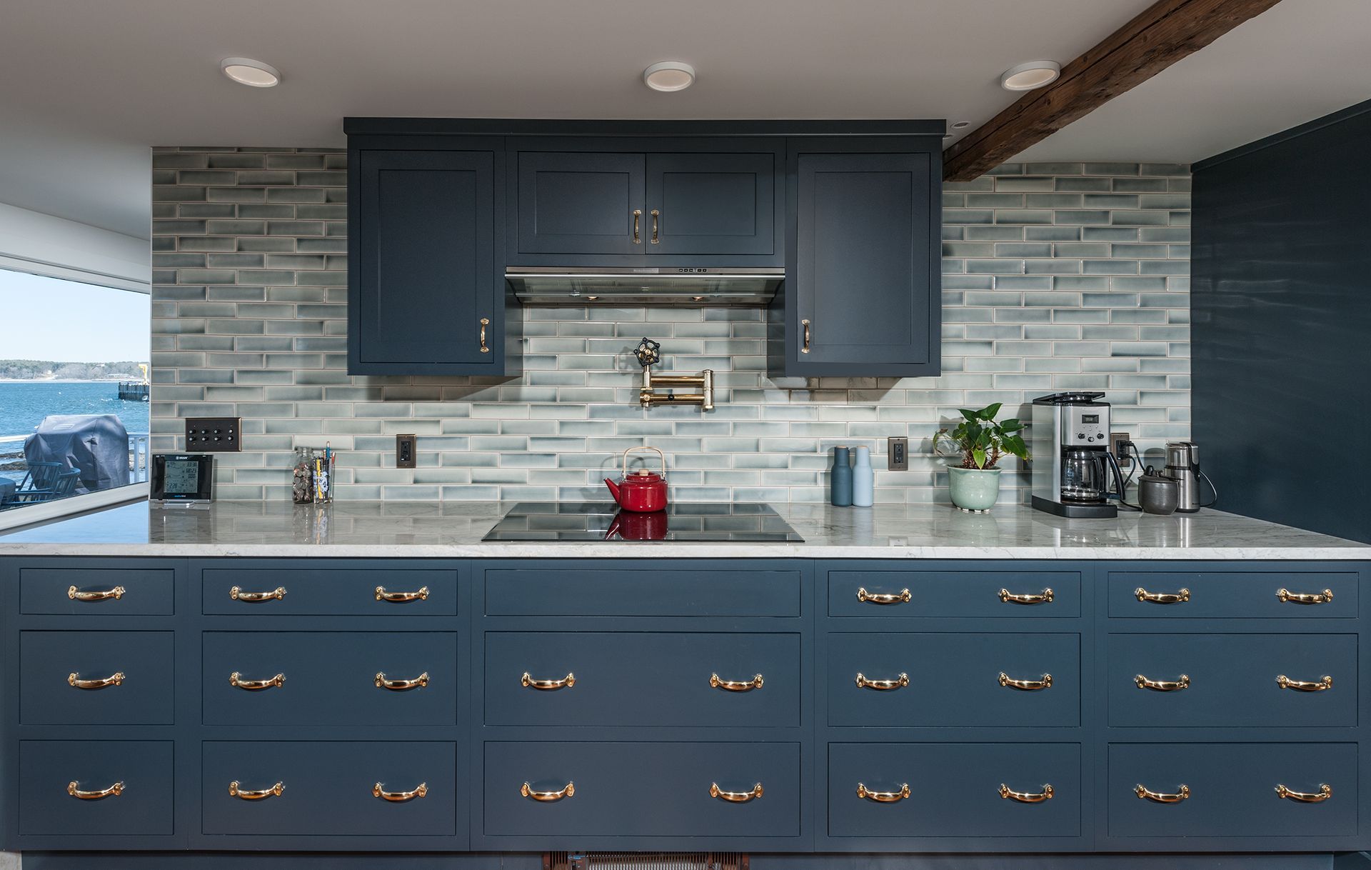 Blue kitchen with brass handles, gray tile backsplash, and countertop decor under dark cabinets