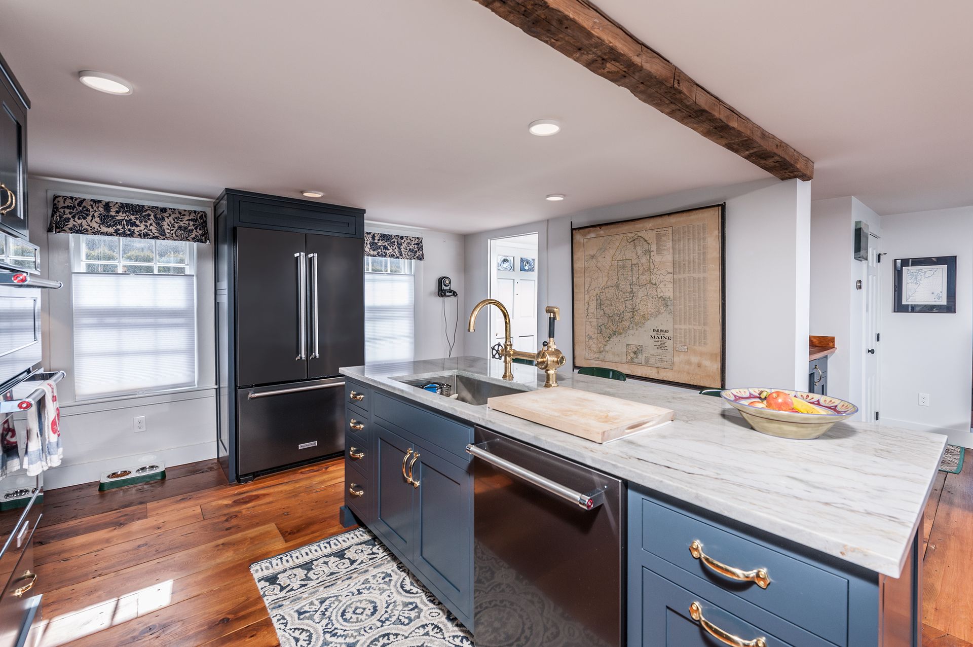 Modern kitchen with blue island, black fridge, white countertops, hardwood floors, and exposed ceiling beam