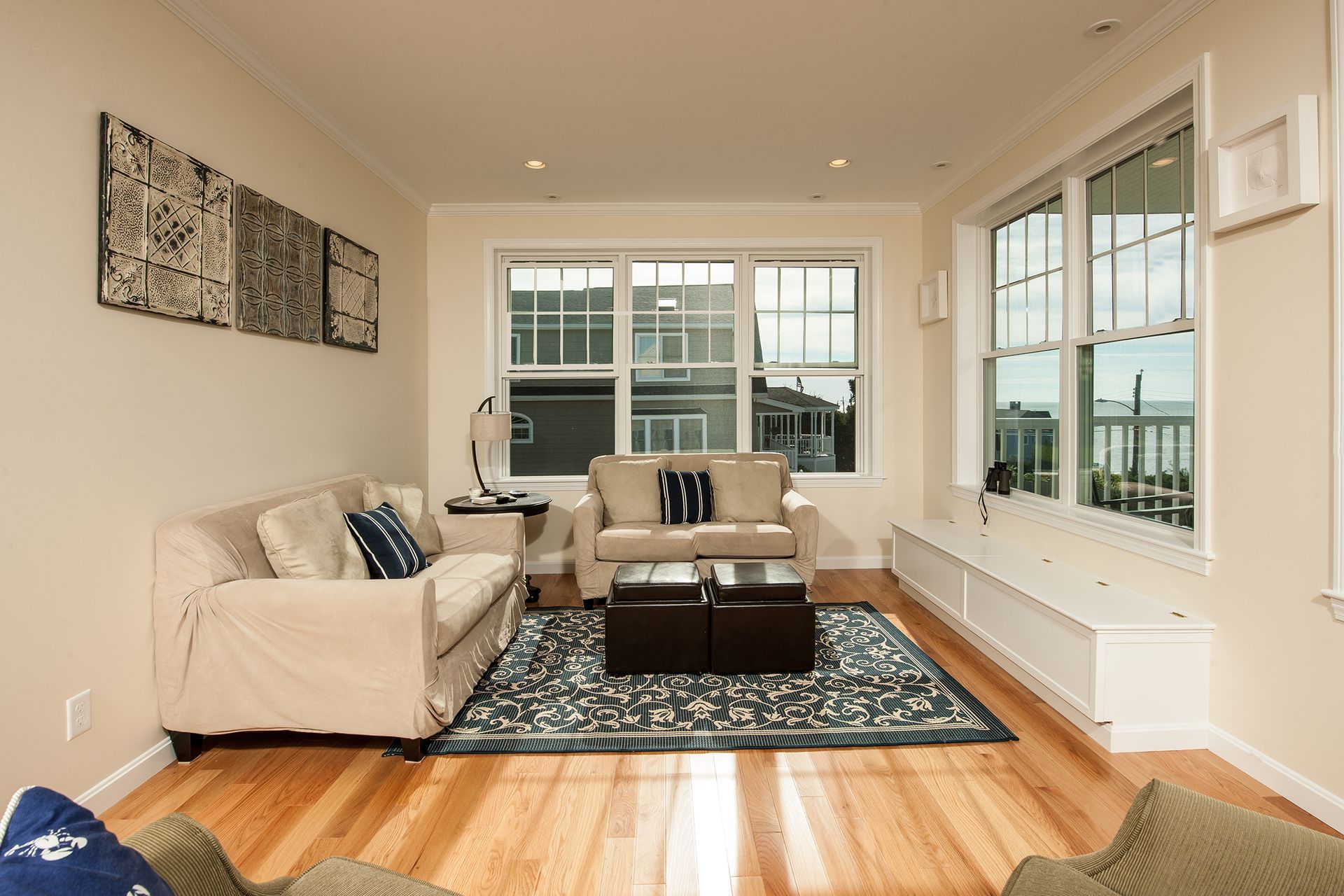 Bright living room with white sofas, dark rug, wood floors, and large windows overlooking water