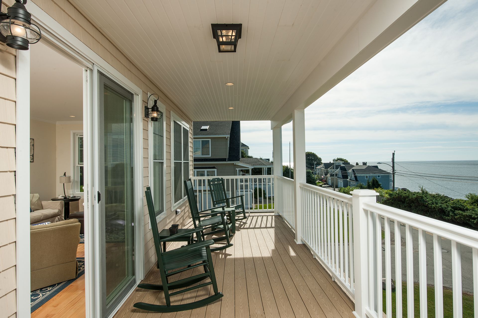 Covered seaside porch with white railing, rocking chairs, and ocean view at sunset