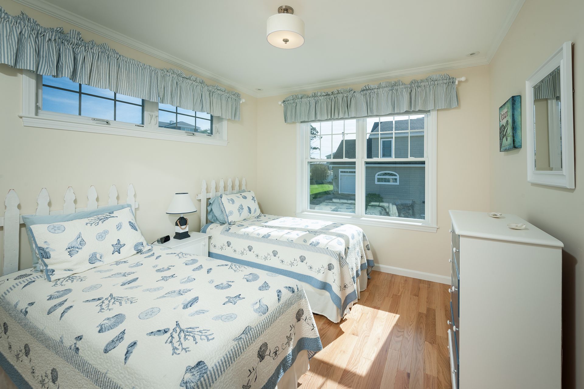 Bright bedroom with two twin beds, blue floral bedding, and large windows with valances.