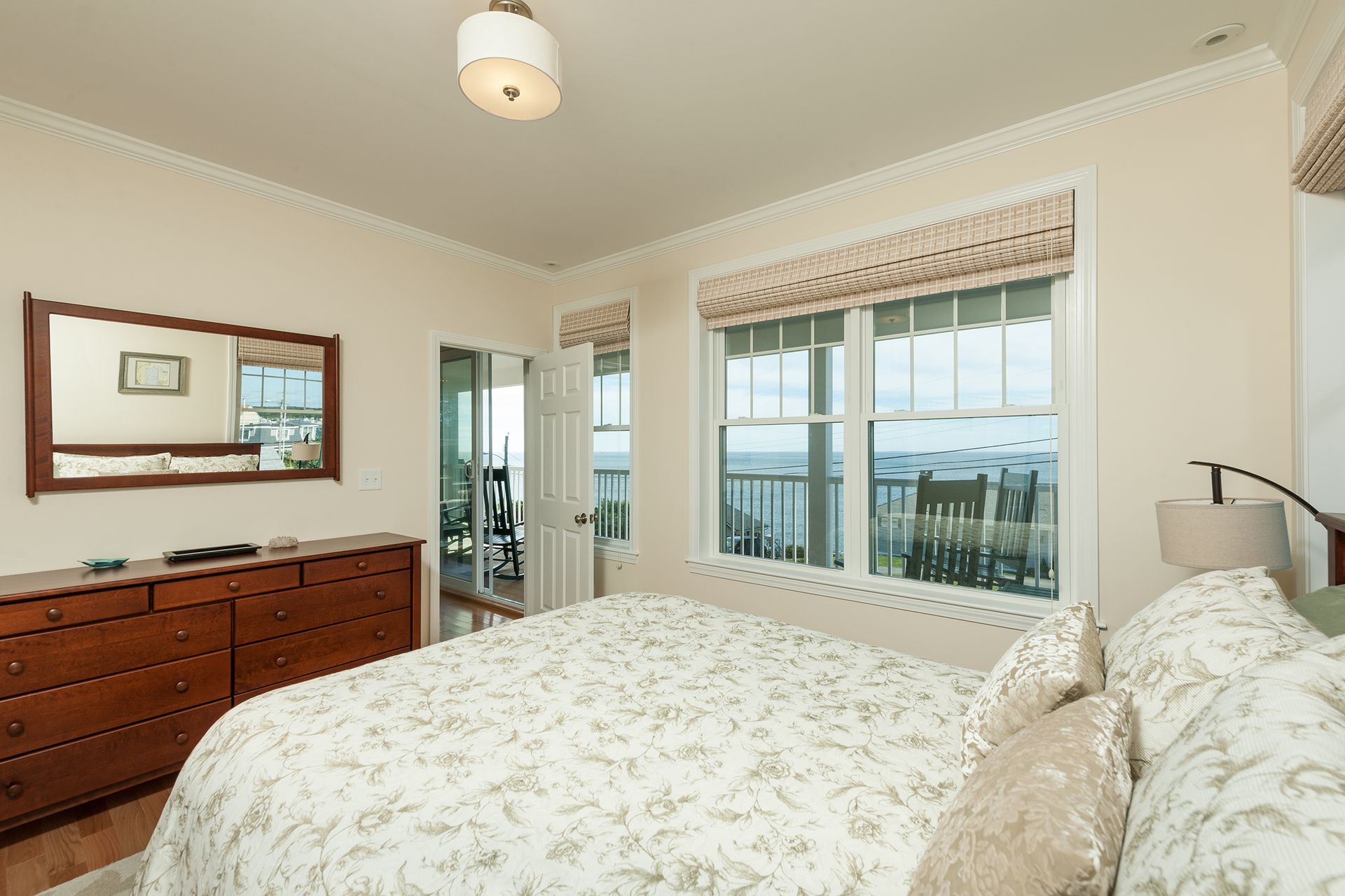 Bright bedroom with floral bedspread, dresser, and ocean-view windows