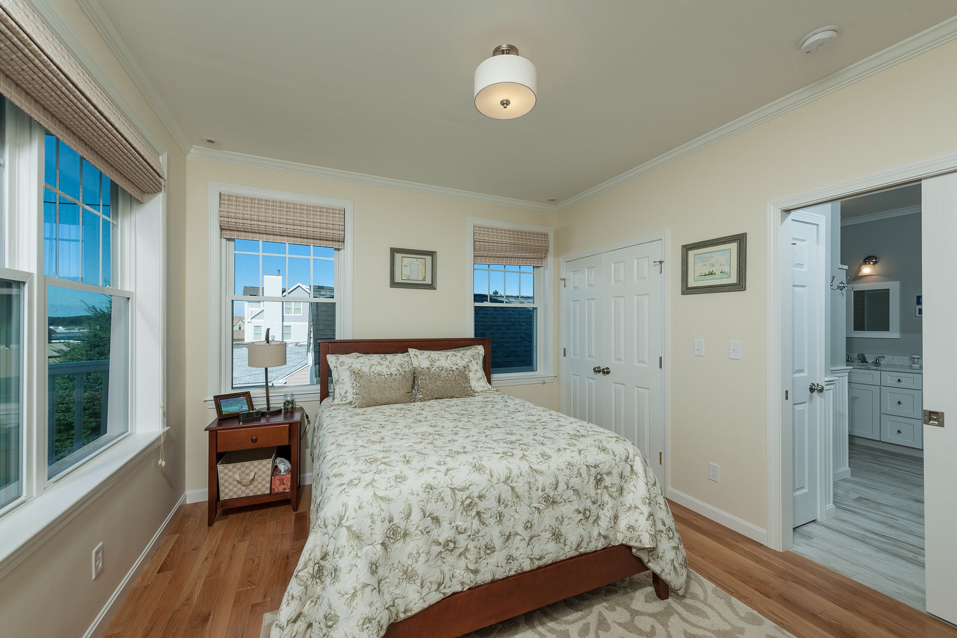 Bright bedroom with a bed, wooden floors, and mirrored closet doors near a bathroom.