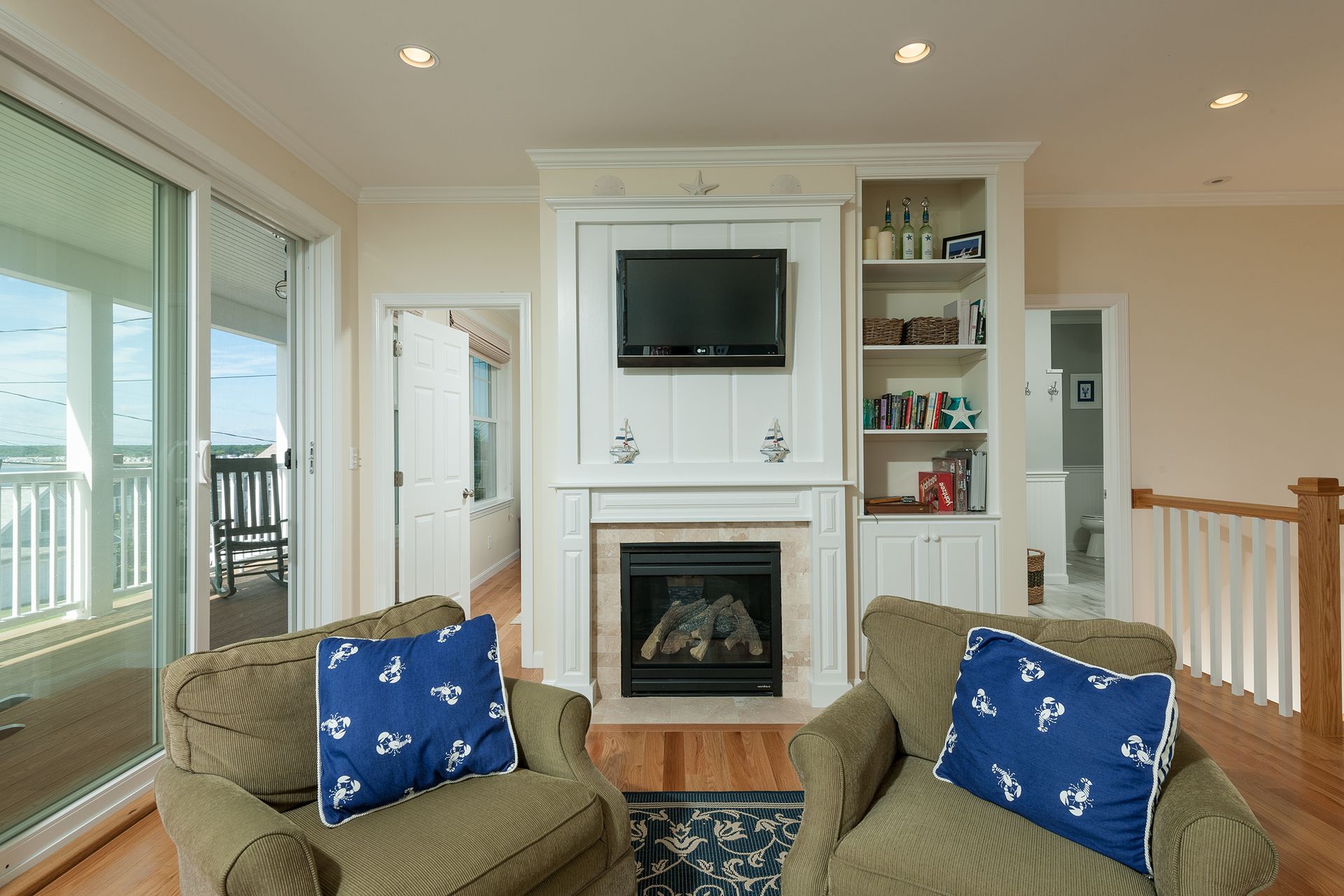 Bright living room with fireplace, wall-mounted TV, and two blue-accented chairs by large windows
